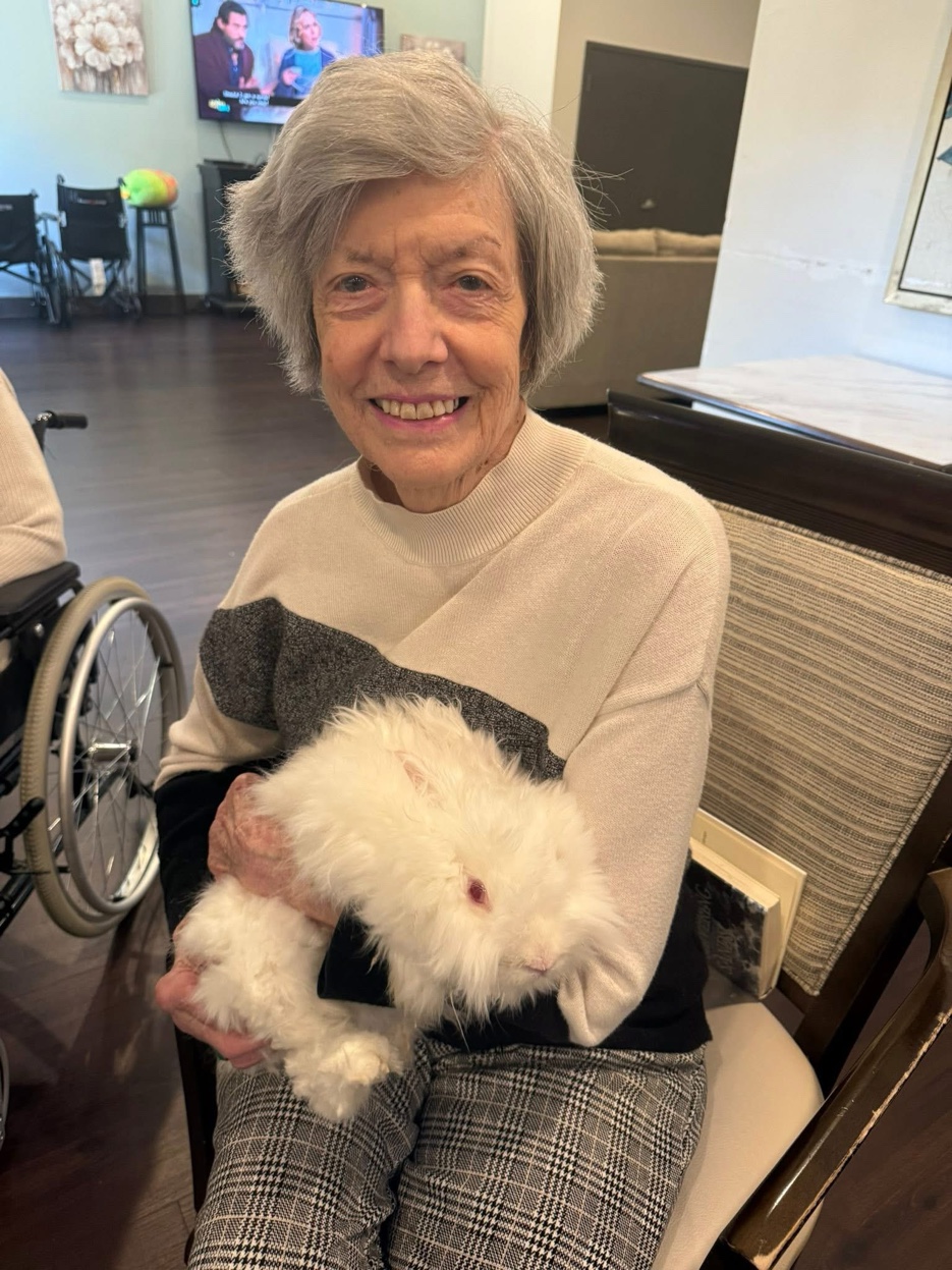 Resident beaming with joy while holding a fluffy white therapy bunny